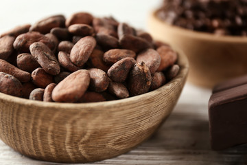 Bowl with cocoa beans on table, closeup