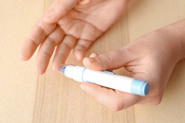 Woman using lancet pen on light background. Diabetes monitoring