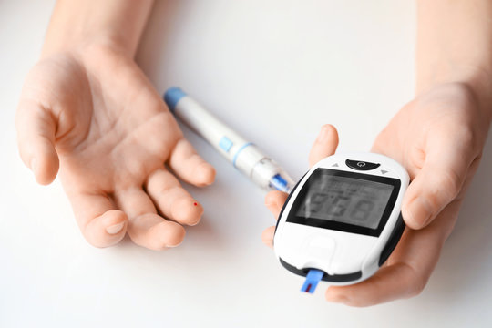 Woman using digital glucometer on light background. Diabetes monitoring