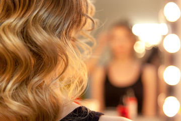 Close up of curly hair and blurred reflection of hairdresser making curls in beauty salon.