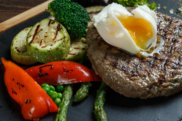 Grilled beef steak cooked on barbecue, closeup on dark wooden table background. Fresh juicy roasted red meat on black stone board, pepper and rosemary. Restaurant food, delicious dish