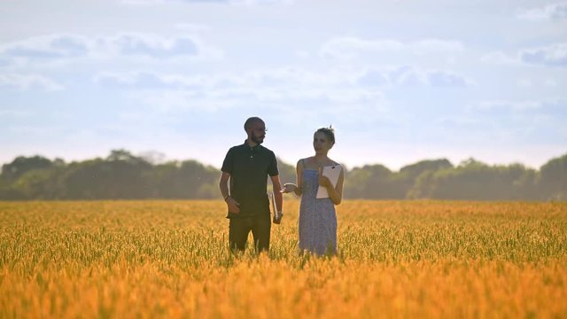 Agriculture engineer walking with female student in wheat field at summer. Agricultural research. Female journalist interviewing agro business man