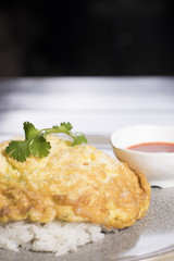 Thai omelette over rice topped with cilantro serve with chili sauce