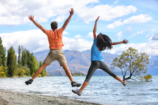New Zealand tourists couple jumping of happiness at Wanaka Lone . Happy young people doing funny jump of joy sightseeing traveling in summer adventure destination. Woman and man.