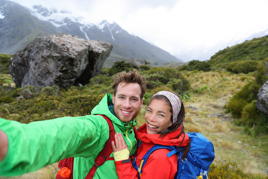 New Zealand travel selfie happy couple backpackers hiking. Travel selfie couple hikers taking smartphone picture on outdoor trail hike in outdoor nature. Active healthy happy people.