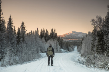 Man standing on snowy road facing mountain at winter sunset