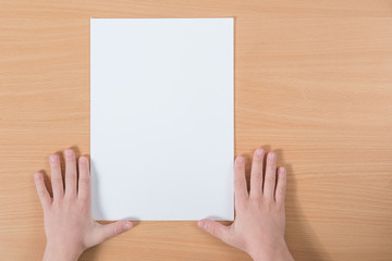 Obraz premium blank sheet of paper with place for your text lying on the table with the hands of a child