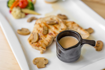 Grilled chicken steak with small mushroom and muchroom sauce in the white dish in the natural light in restaurant.