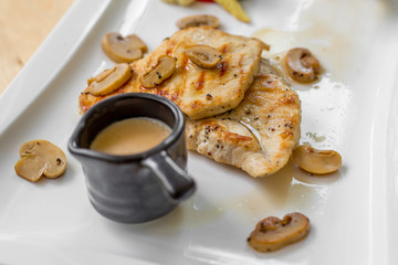Grilled chicken steak with small mushroom and muchroom sauce in the white dish in the natural light in restaurant.