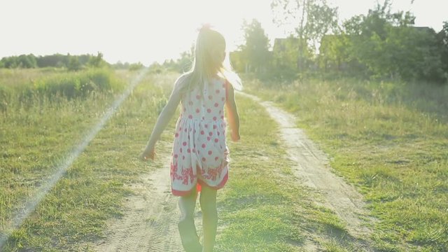 Little girl in a white sundress with red patterns running along a country road, jumps and flips in the air