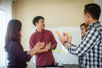 Handsome young man standing near whiteboard and pointing on the chart presentation perfect planning business with people group clapping.