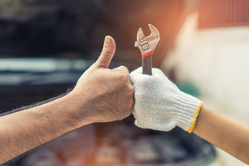 Mechanic hand checking and fixing a broken car in  garage.hand of mechanic with thumbs up and tool