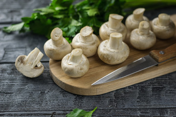 Fresh sliced mushrooms on chopping Board and parsley on dark wooden table.