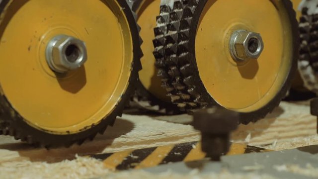 Rolling spiked wheels of plank refiner machine working on wood at carpenter production, close up