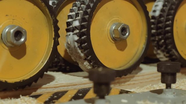 Spinning spiked wheels of plank refiner machine working on wood at carpenter factory, close up