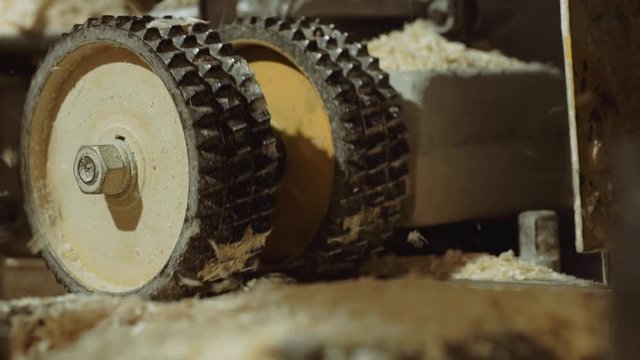 Rolling spiked wheels of board refiner machine working on wood at carpenter factory, close up