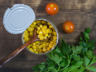 Canned corn in an open aluminum cans and parsley on a wooden table. The view from the top.