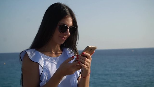 Beautiful brunette girl in little blue dress taking pictures of herself at the background of the sea and rocks in Cyprus