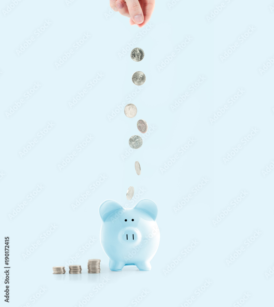 Wall mural female hand putting coin into piggy bank on pastel blue background