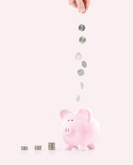 Female hand putting coin into piggy bank on pastel pink background