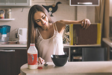 young beautiful woman breakfast  pours  cereal from  box into  bowl