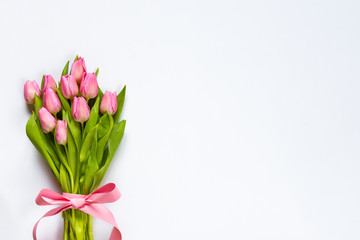 Top view of pink tulips bouquet, wrapped with pink ribbon over white background. Copy space.