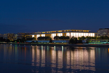 Washington DC night panorama with John F. Kennedy Center for the Performing Arts in the center of the frame. Brightly lit The Kennedy Center with reflection in dark waters of Potomac River.
