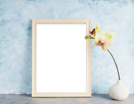 Bright photoframe mockup with yellow orchid against  light blue wall. Interior design concept. Text space