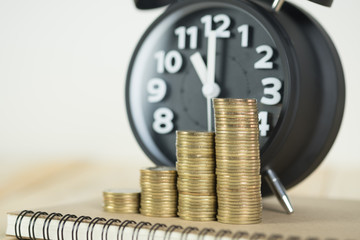 Steps of coins stack with vintage alarm clock and pen, notebook paper on wooden working table with copy space for text, financial and business planning concept..