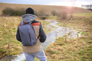 Tourism. Traveler with a backpack looks at the stream. Hiking in the spring
