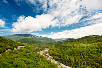 Scenic mountain landscape with green hills and the river between the mountains, blue sky with clouds. The Caucasus Mountains, Georgia, Europe. Nature and travel background.