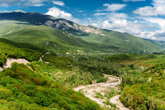 Scenic mountain landscape with green hills and the river between the mountains, blue sky with clouds. The Caucasus Mountains, Georgia, Europe. Nature and travel background.