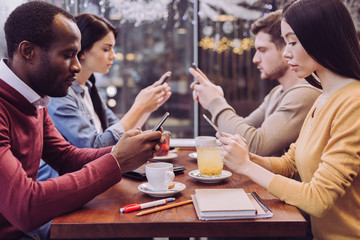 Absence of communication. Nice busy four friends using phones while sitting at cafe and looking down