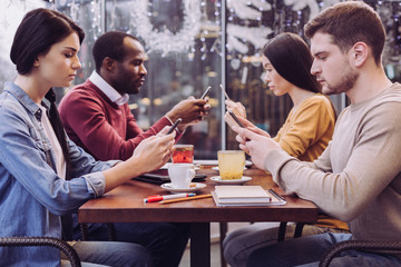 Interpersonal distance. Nice melancholic four friends staring at phones while gathering at cafe and keeping silence