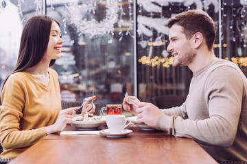 Love time. Happy merry young couple eating salads while laughing and sitting in front of each other