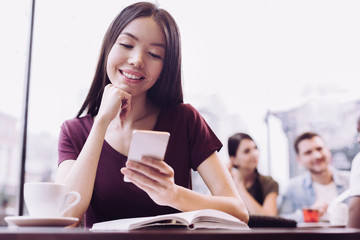 Phone call. Optimistic attractive female student using phone while placing head on hand and looking down