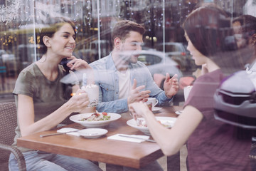 Time for friends. Happy pleasant three friends chatting while eating salad and laughing