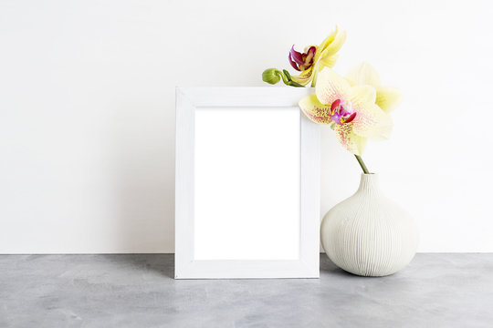Bright photoframe mockup with yellow orchid against white wall. Interior design concept. Text space