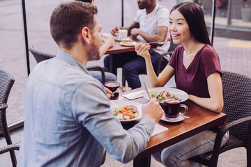 Lovely atmosphere. Top view of sincere young happy couple posing at cafe and woman eating salad while grinning