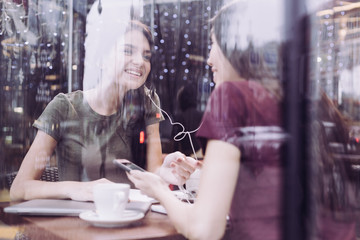 Music choice. Merry gay female students listening to a song while sitting at cafe and have fun