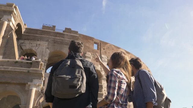 Three young friends tourists standing in front of colosseum in rome with backpacks sunglasses happy beautiful girl long hair