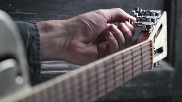 closeup perspective view of Caucasian young man hand tuning and playing on acoustic Dobson metal guitar on dark background