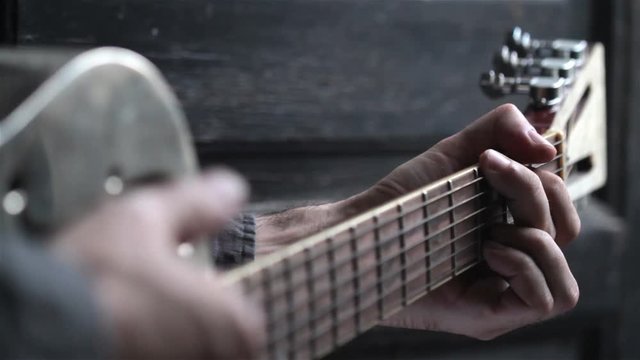 closeup perspective view of Caucasian young man hand playing on acoustic Dobson metal guitar on dark background