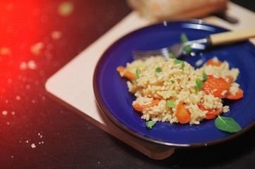 Pilaf of rice with apricots, mint leaves, in a dark blue plate on a wooden Board on black background.