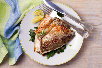 Roasted sea bream with spinach. Dorado or dorada fish fillet on white plate