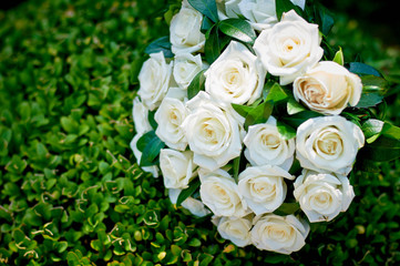 white roses bouquet with periwinkle twigs on green leaves background 