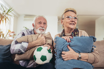 Happy senior couple watching soccer on tv and celebrating victory at home