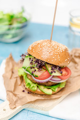 Tasty vegan burger with fresh vegetables on dark rustic wooden table, selective focus. Healthy fast food background with space for text.