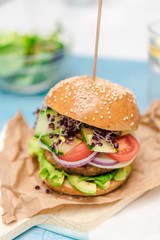 Tasty vegan burger with fresh vegetables on dark rustic wooden table, selective focus. Healthy fast food background with space for text.