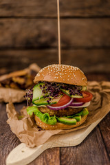 Tasty vegan burger with fresh vegetables on dark rustic wooden table, selective focus. Healthy fast food background with space for text.